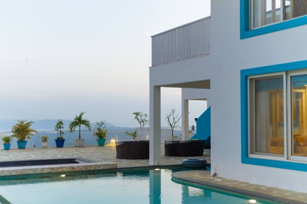 A modern building with a pool, outdoor seating, and a view of the sea.