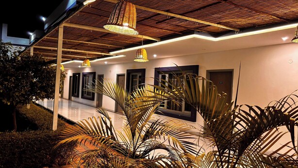 L’extérieur d’un hôtel moderne, de nuit, avec une galerie couverte, de grandes fenêtres et des guirlandes lumineuses.