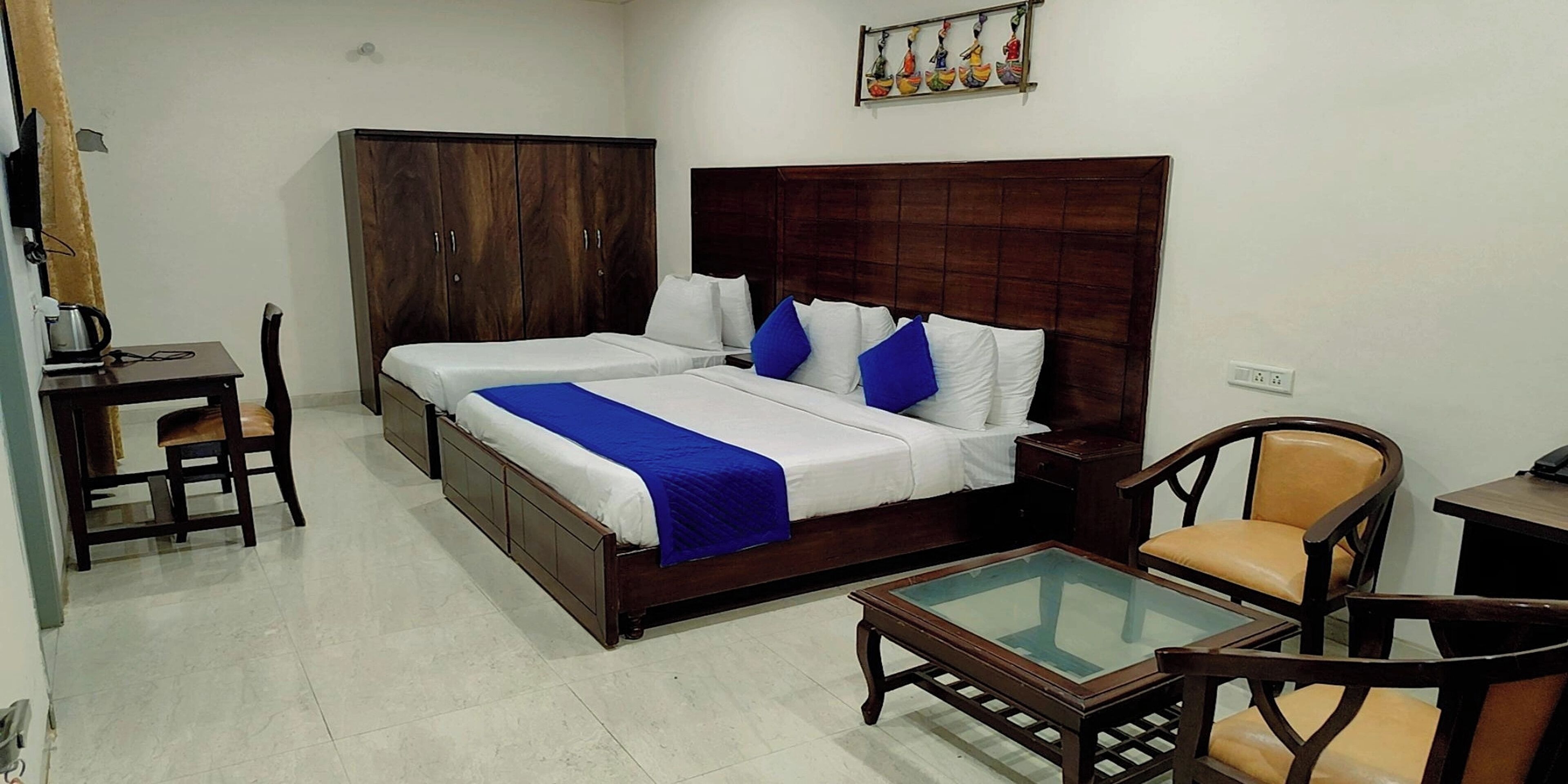 A bedroom with a double bed, a wooden wardrobe, a small table with a glass top, and a chair.