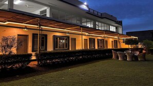 Un bâtiment moderne doté d’un toit plat, de grandes fenêtres et d’un espace extérieur couvert aménagé avec des chaises et des tables.