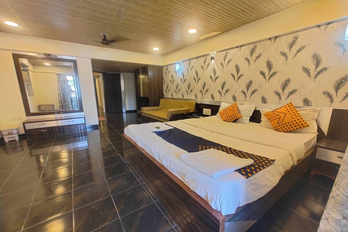 A hotel room with a large bed, a wooden ceiling, a mirror, a sofa, and a patterned wall.