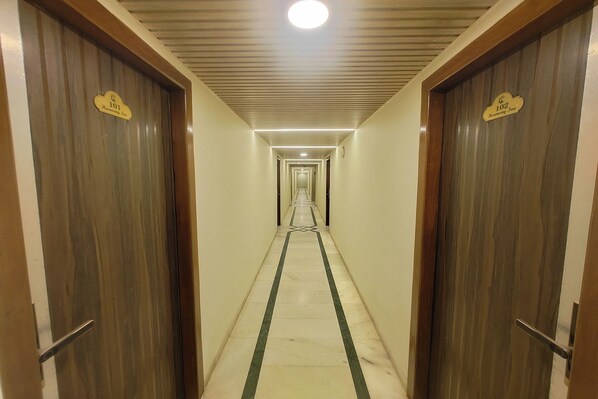 A long, narrow hallway with wooden doors on either side, each marked with a number. - Harmony Inn (Mahabaleshwar)