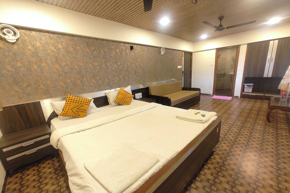 A hotel room with a large bed, a sofa, a desk, and a wardrobe.