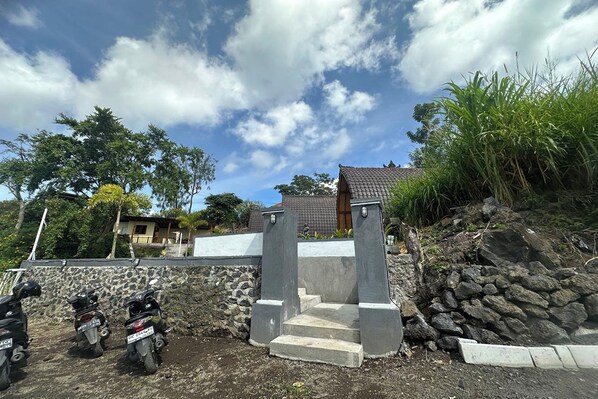 A stone staircase leading to a house with a tiled roof, surrounded by vegetation and parked motorcycles. - Nirwana Kintamani (Kintamani)