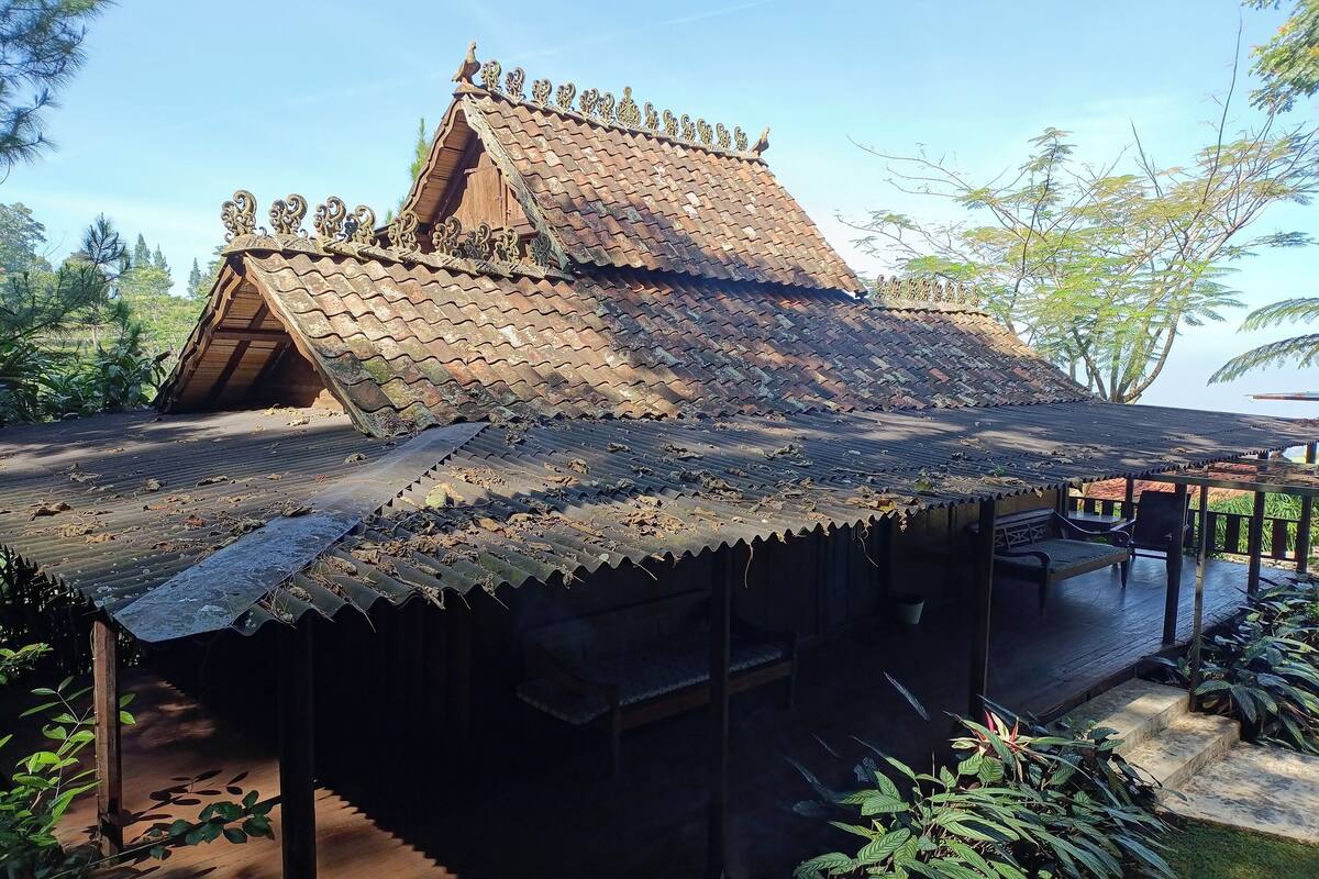 Ein traditionelles Haus mit geneigtem Dach, Holzbauweise und einer Veranda mit Sitzgelegenheit.