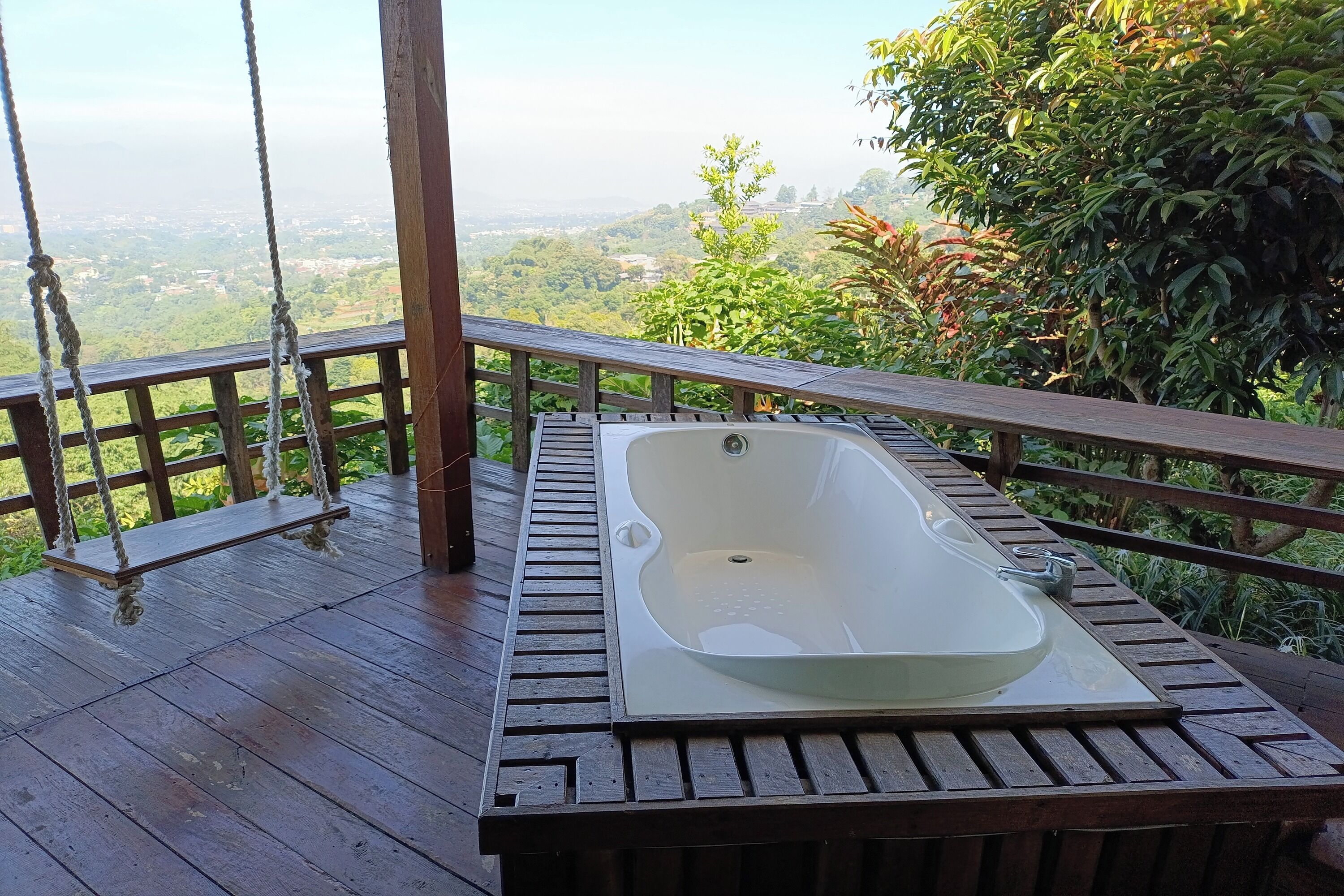 A wooden deck with a swing and a hot tub.