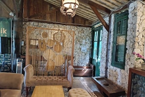 A rustic interior with stone walls, wooden furniture, and a decorative hanging screen. - Mendulang By Belza By Zuzu (Lembang)