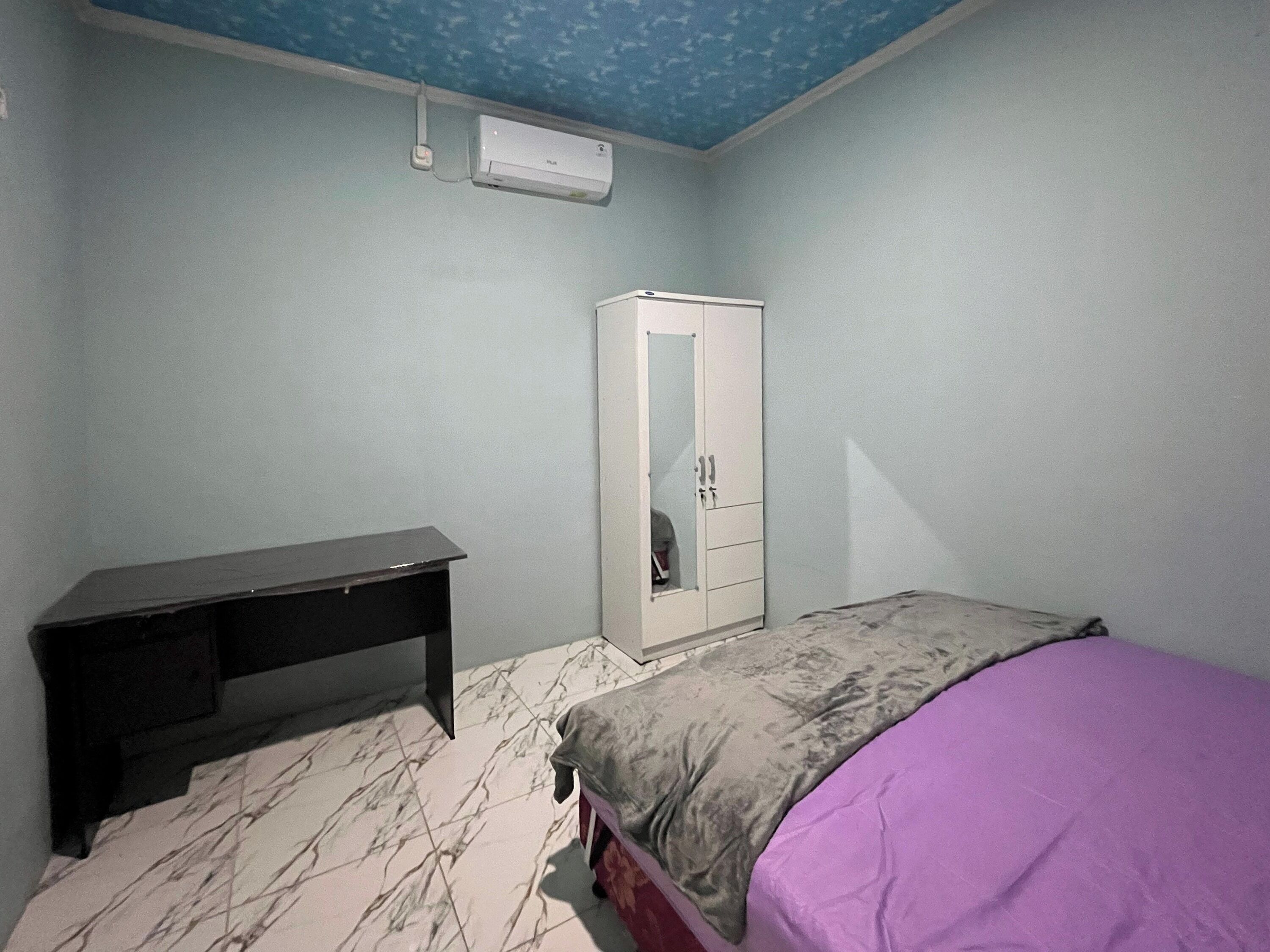 Et soveværelse med seng, skab, skrivebord og aircondition i loftet.