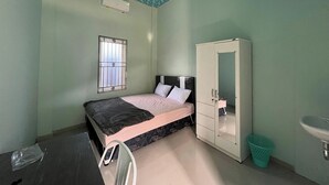 Ein Schlafzimmer mit Bett, Kleiderschrank, einem Fenster mit Gitterstäben, einem Waschbecken und einem Mülleimer.