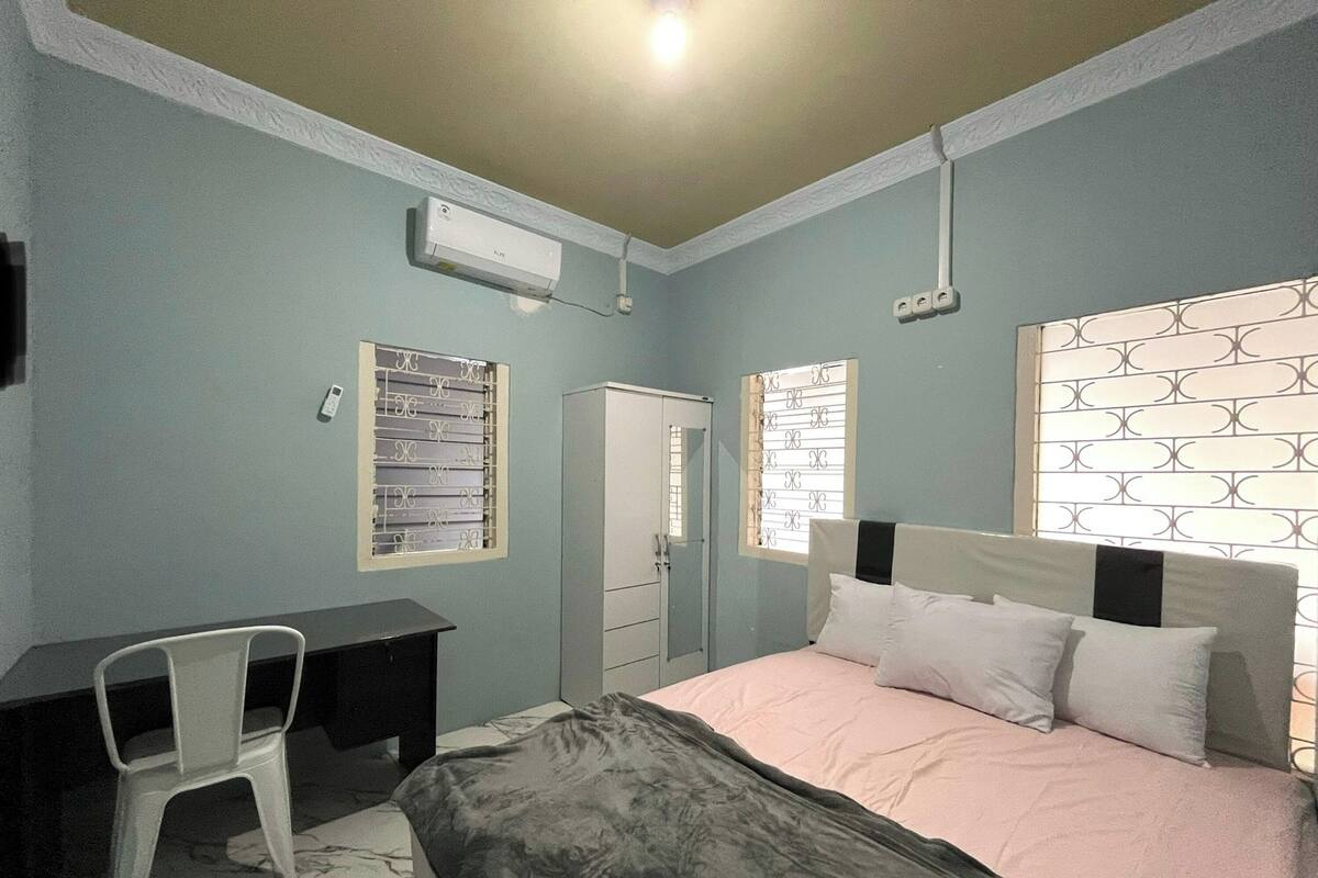A bedroom with a bed, a desk, a chair, a wardrobe, and a window with a decorative screen.