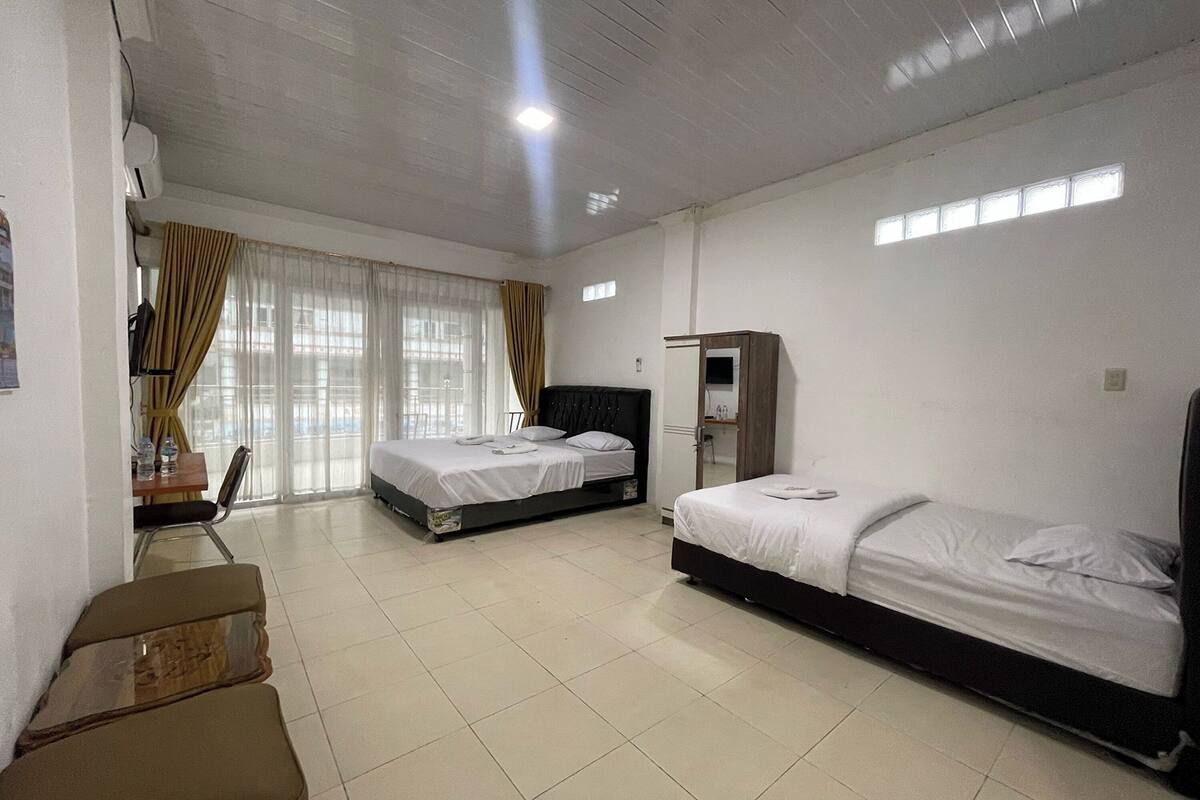 A hotel room with two beds, a desk, a chair, a wardrobe, and a window with curtains.