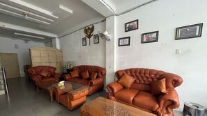 Un salon avec des canapés en cuir marron, une table basse en verre et une table basse en bois. Des tableaux encadrés ornent le mur, et un ventilateur de plafond est installé au plafond.