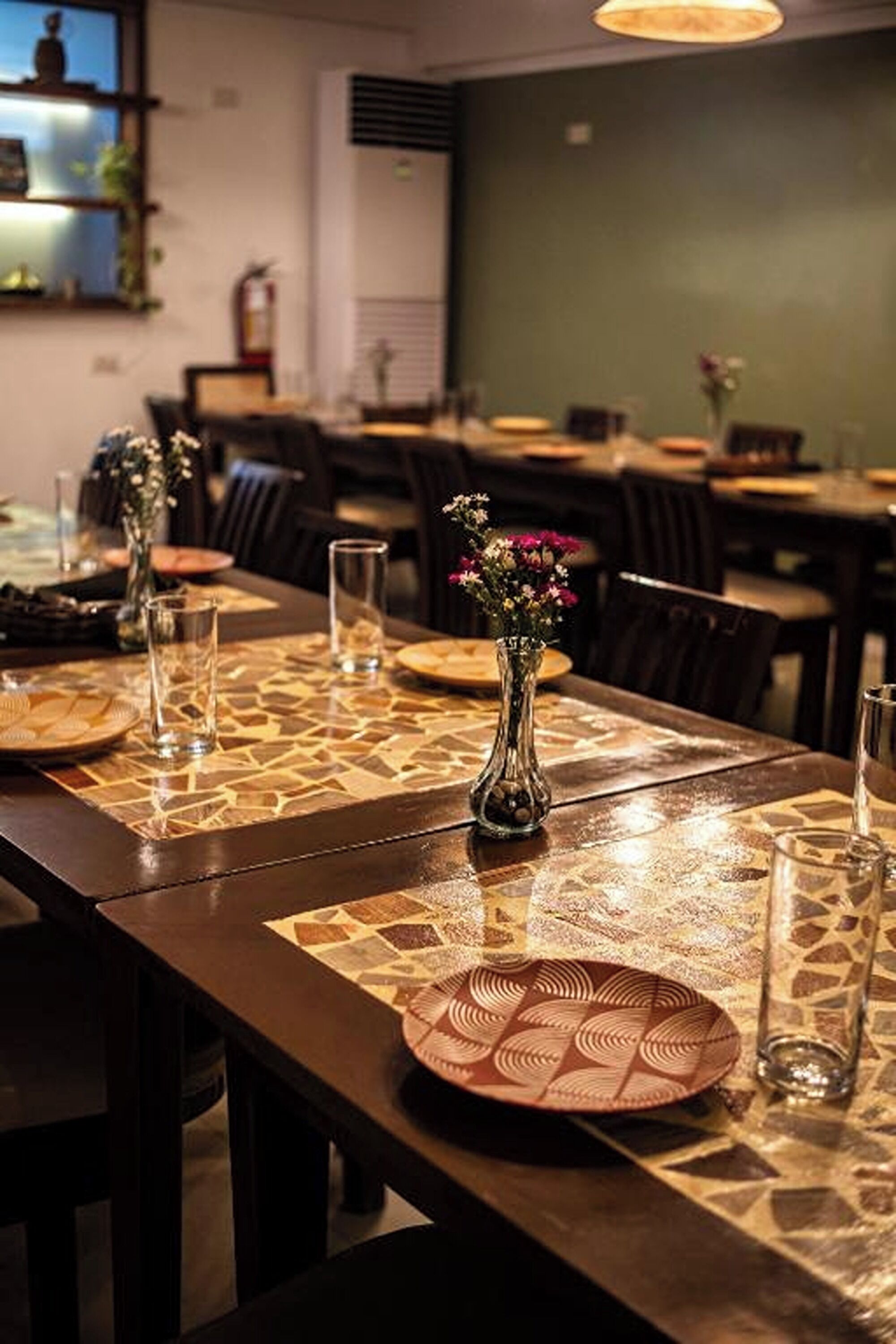 A dining area with tables set for meals, featuring patterned placemats and a vase with flowers.