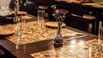 A dining area with tables set for meals, featuring patterned placemats and a vase with flowers.
