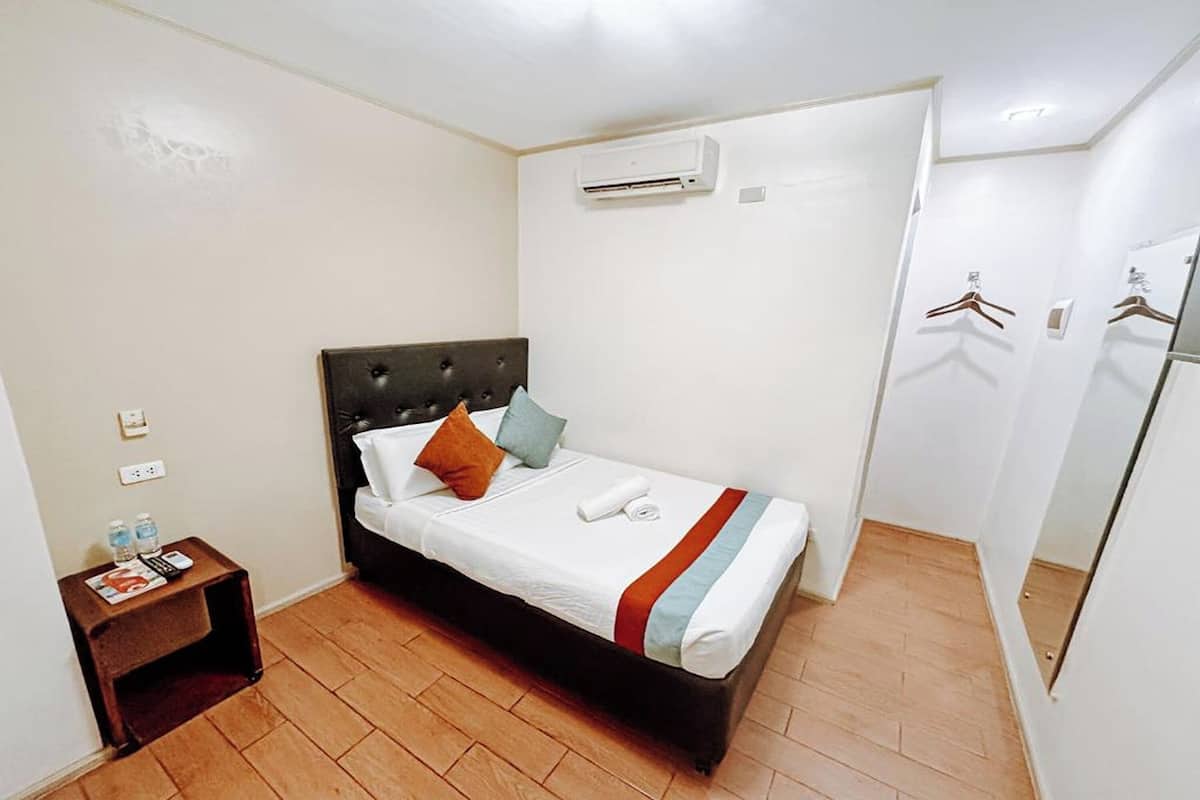 A compact hotel room with a single bed, a small bedside table, an air conditioning unit, and a wardrobe with hanging space.