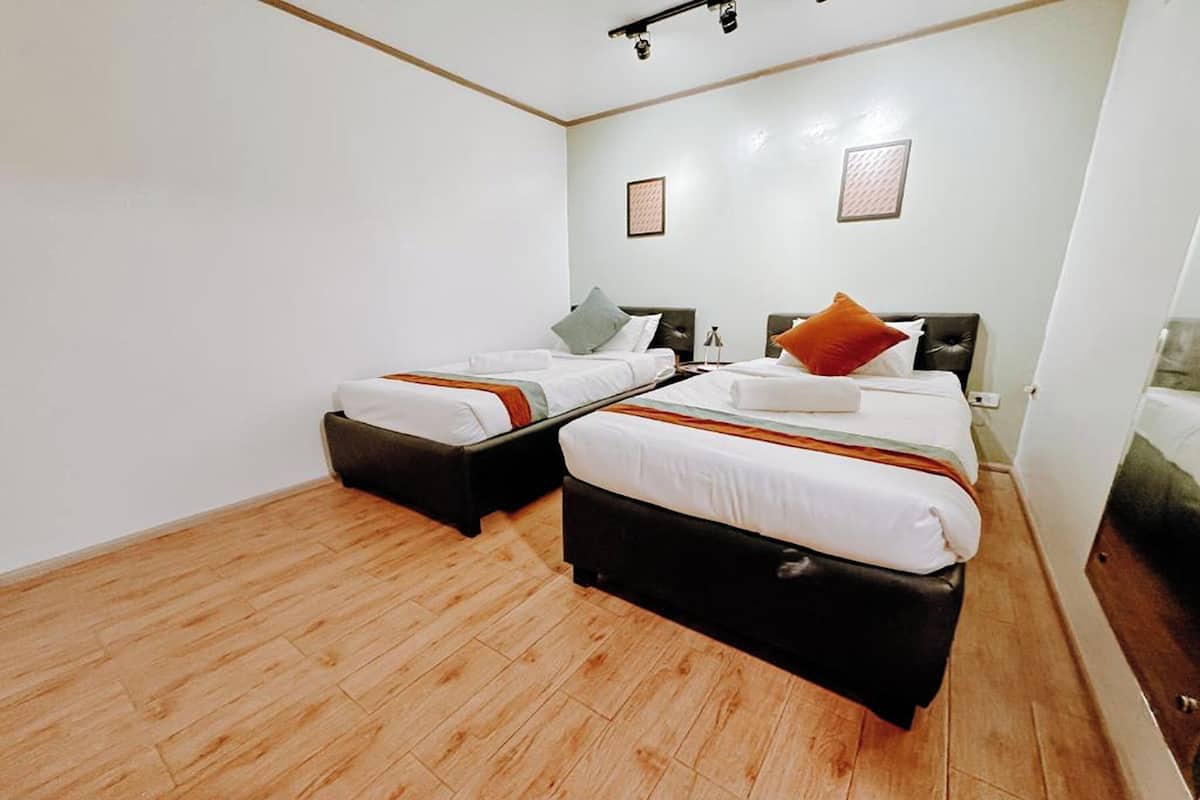 A room with two beds, wooden flooring, and a white wall with two framed pictures.