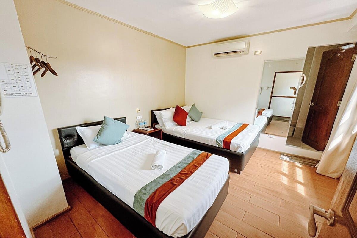 A hotel room with two beds, a wooden floor, a mirror, and a door.