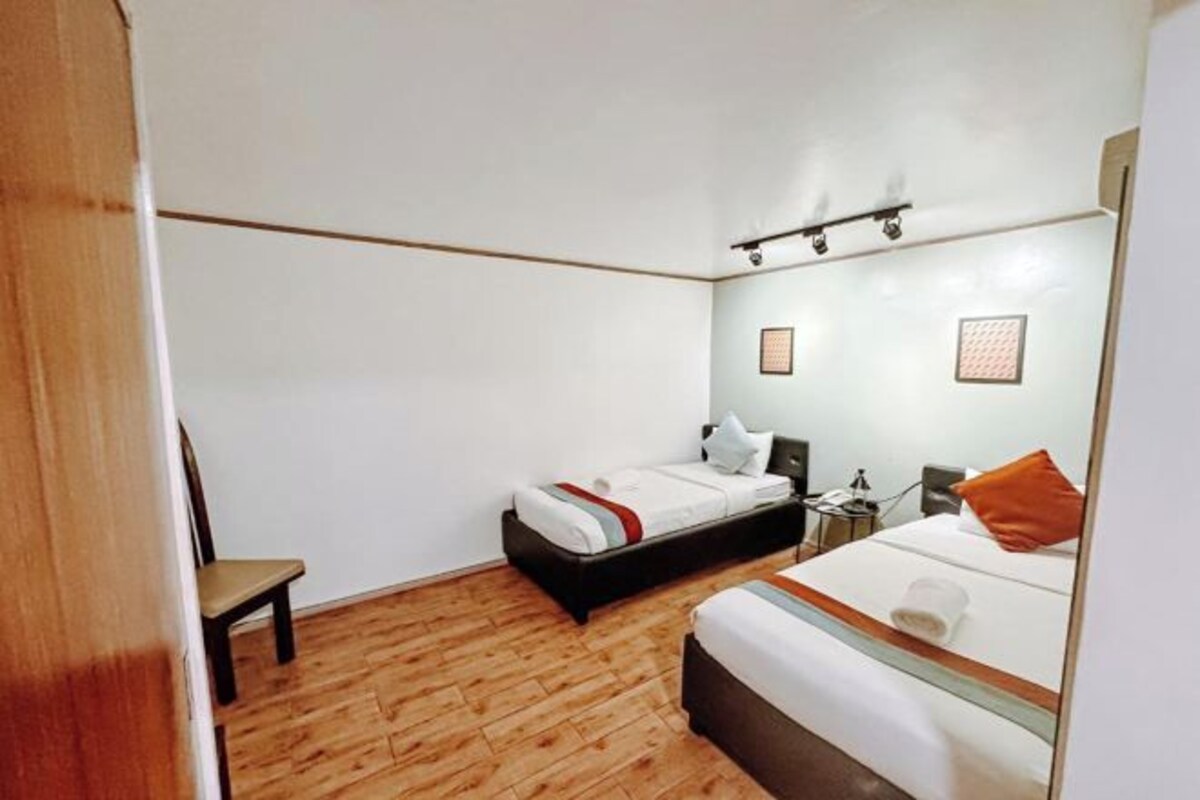 Hotelkamer met houten vloer, twee bedden, een stoel, nachtkastje en een klein bureau met lamp.