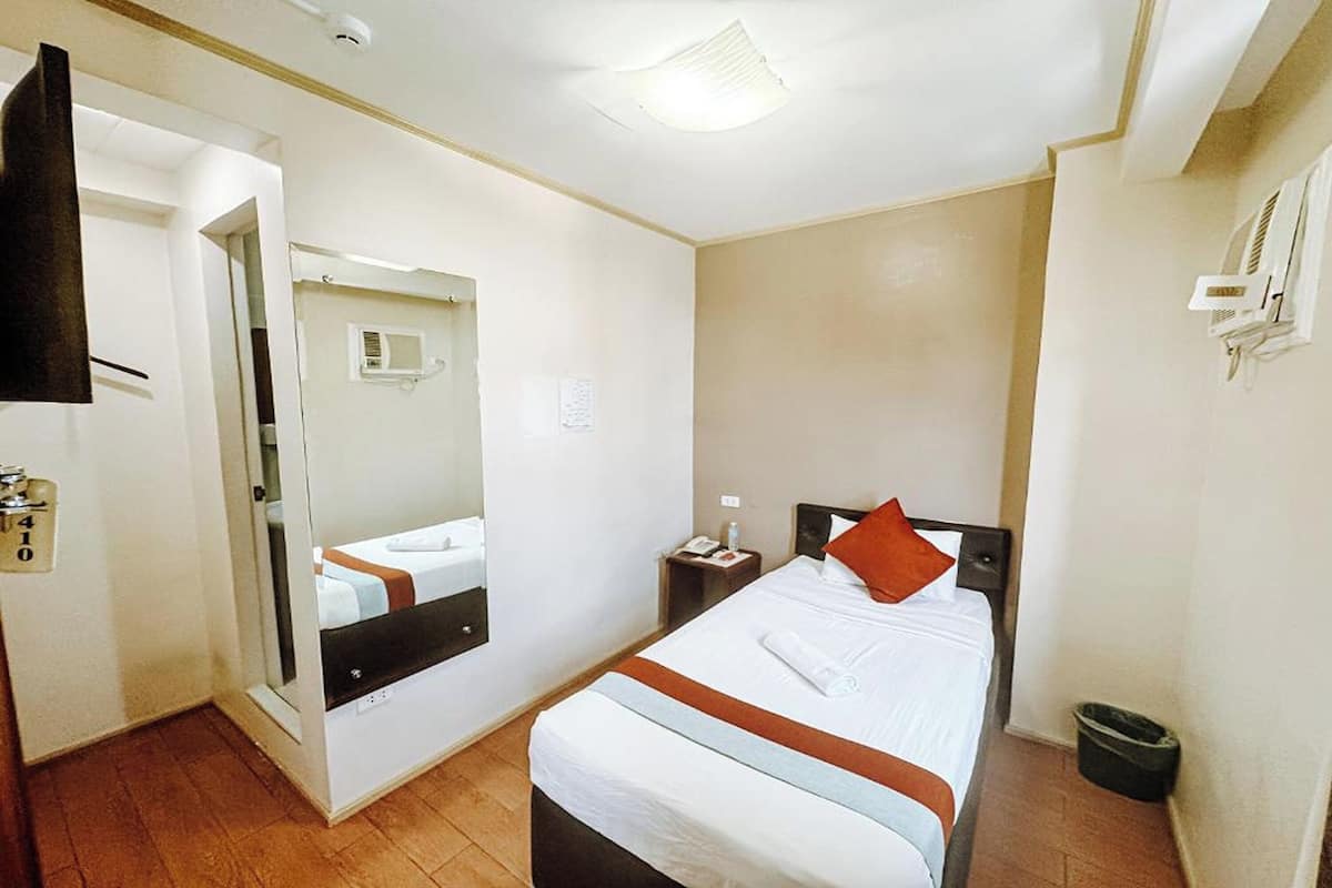A hotel room with a bed, a bedside table, a mirror, a door, and a small trash bin.