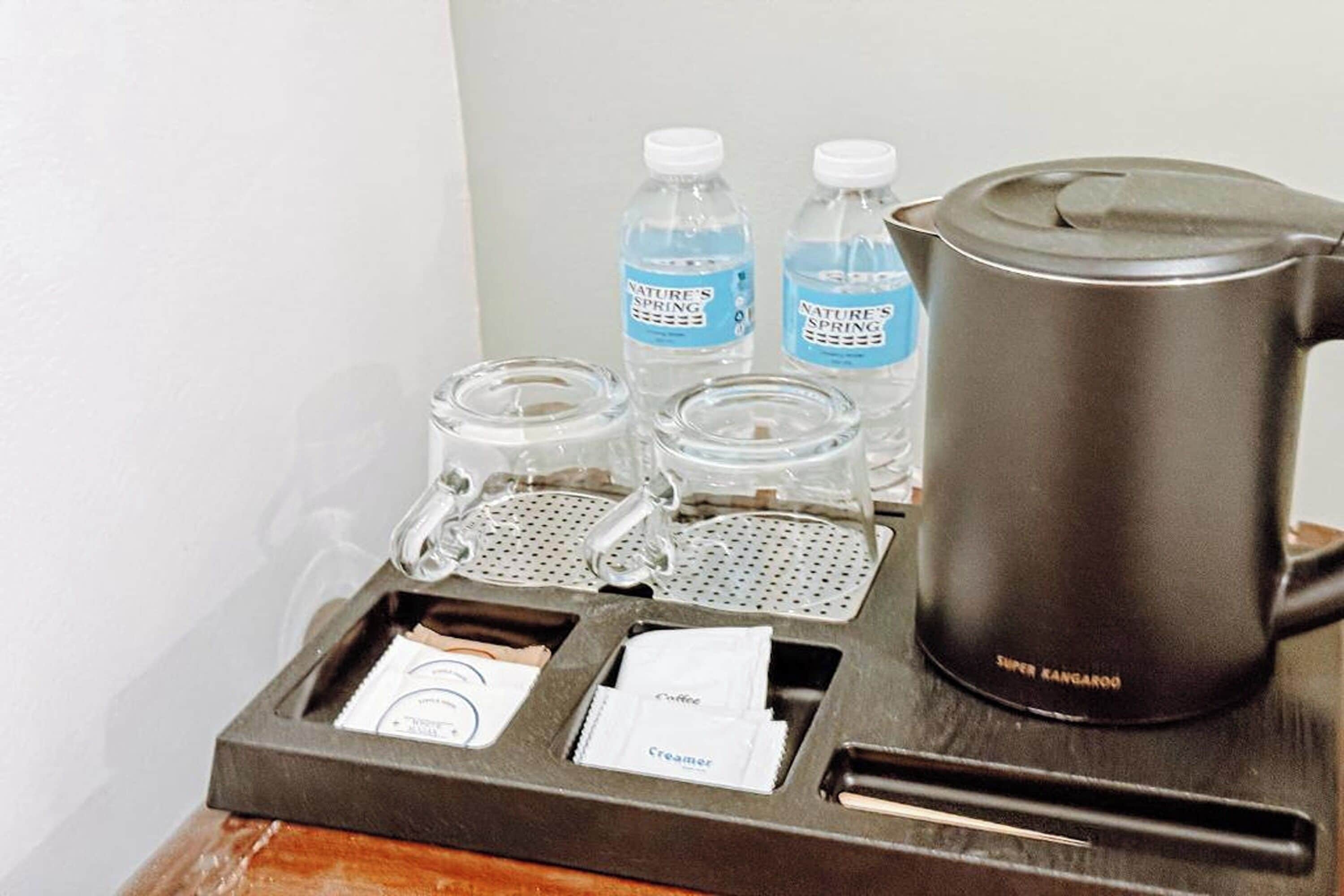A coffee station with a black coffee pot, two water bottles, and a tray with coffee and creamer packets.