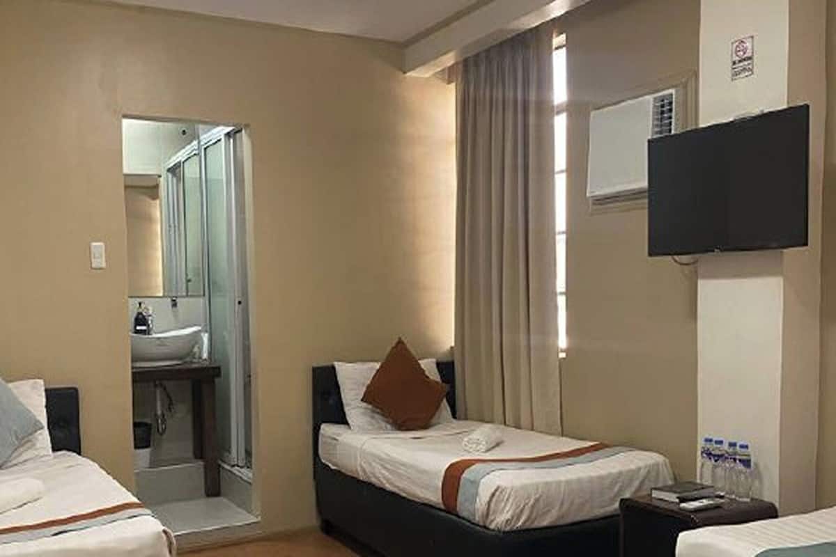 A hotel room with two beds, a bathroom, a flat-screen TV, and a window with curtains.