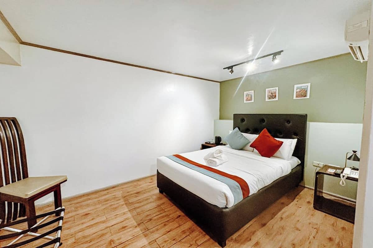 A bedroom with a bed, a nightstand, a chair, and a wall-mounted air conditioner.