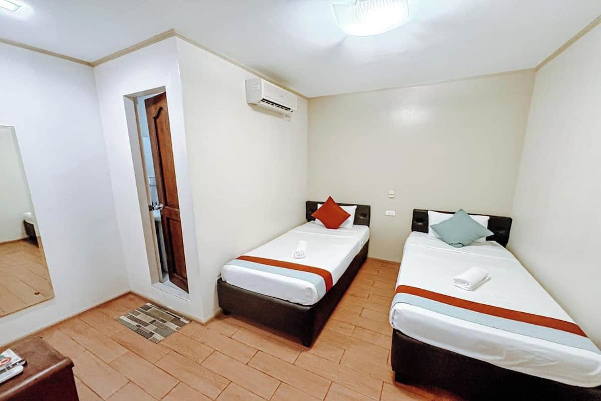 A small, clean room with two beds, a door, an air conditioning unit, and a mirror.