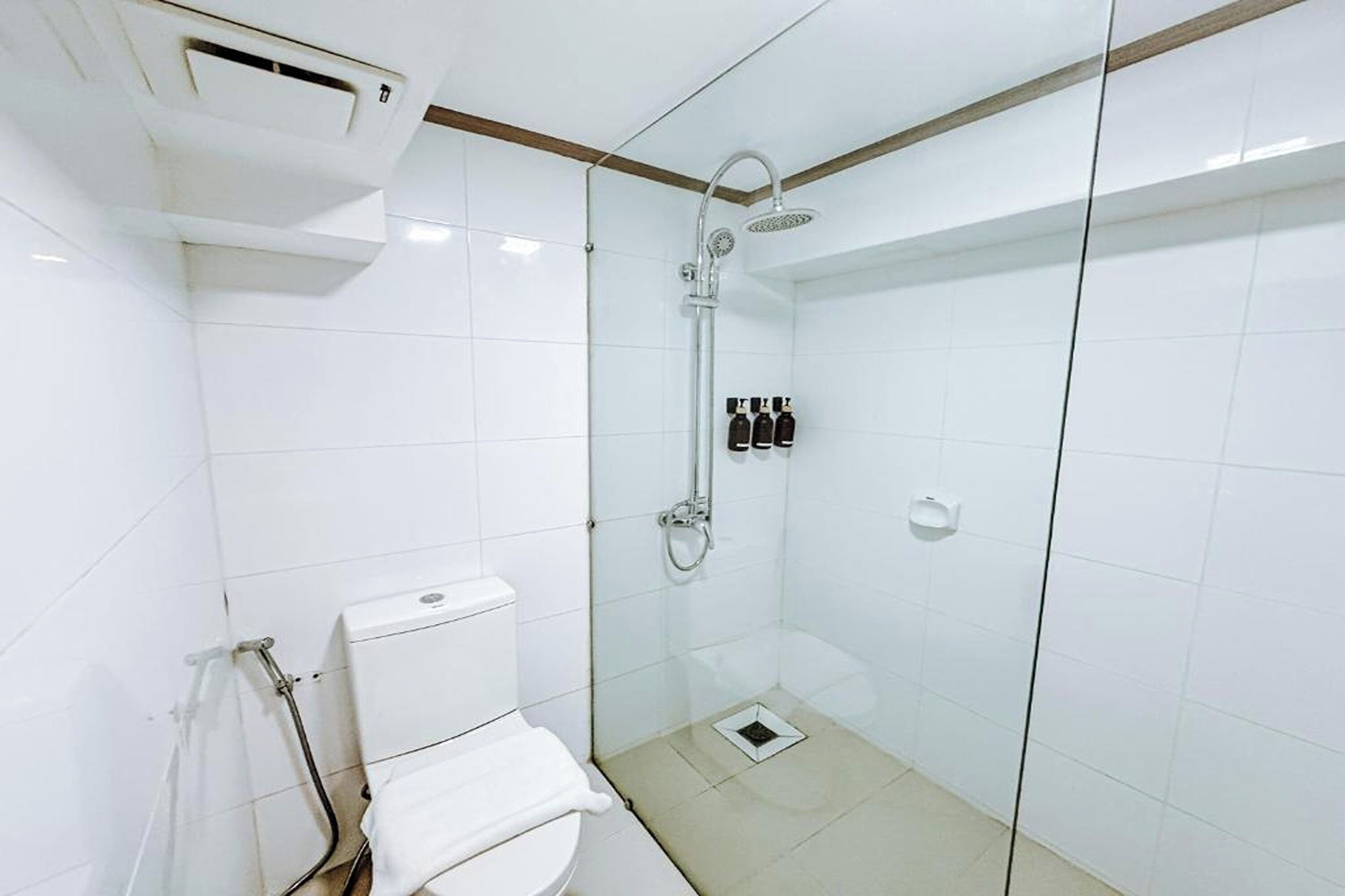 A modern bathroom with a glass-enclosed shower, white tiles, a toilet, and a hand dryer.