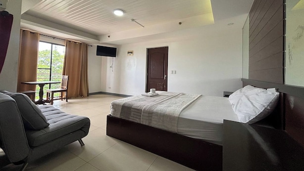 A modern hotel room with a bed, a sofa, a small table, and a TV on the wall. - Yellowbell Hotel (Batangas City)