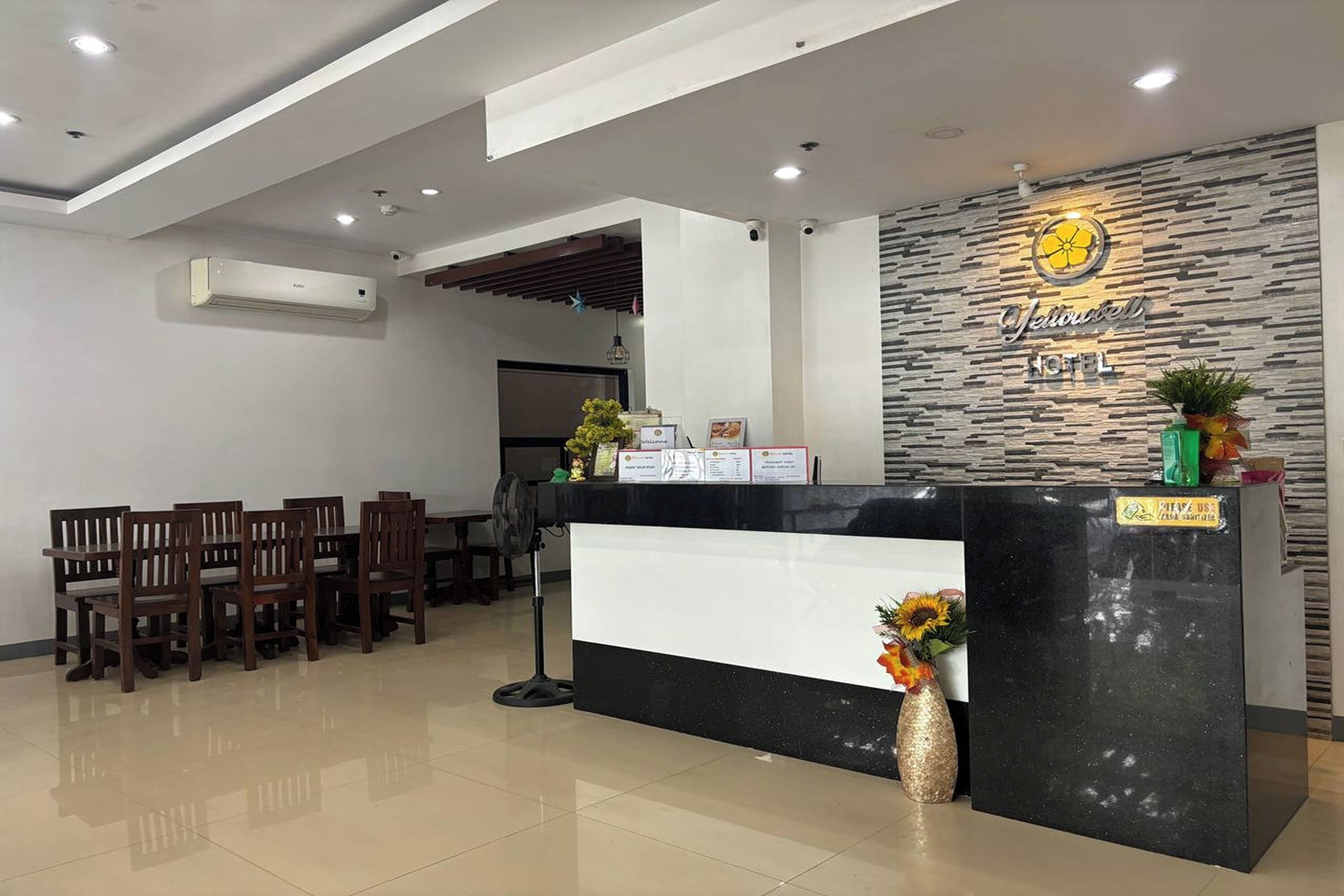 A hotel reception area with a black reception desk, wooden chairs, a wall-mounted air conditioner, and a sign that reads "Jalow Hotel".