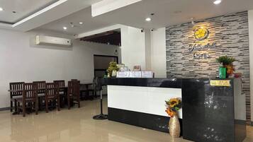 A hotel reception area with a black reception desk, wooden chairs, a wall-mounted air conditioner, and a sign that reads "Jalow Hotel".
