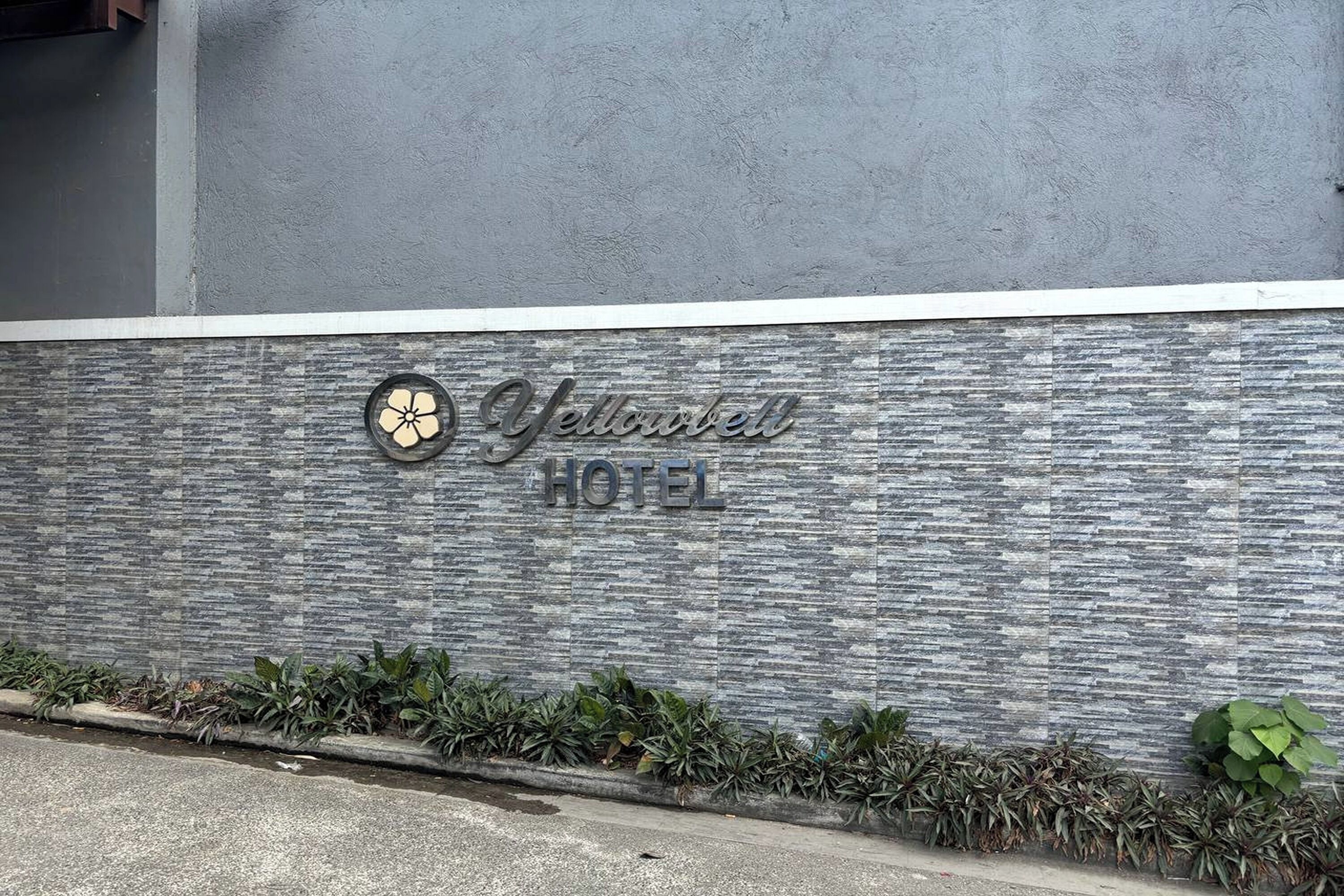 Un letrero de hotel con un logotipo y el nombre 'Yellowbell Hotel' sobre una pared con textura.