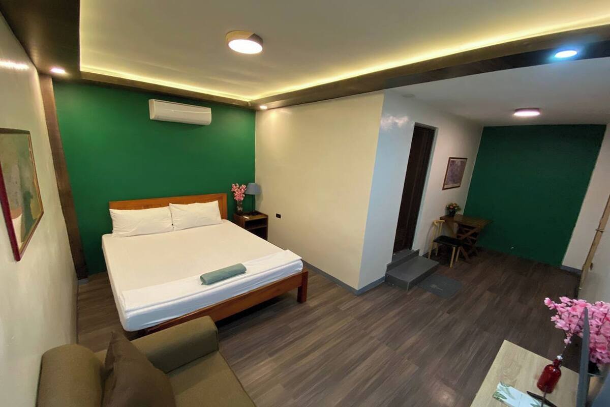 A hotel room with a bed, a sofa, a small table with a vase, and a desk with a chair.