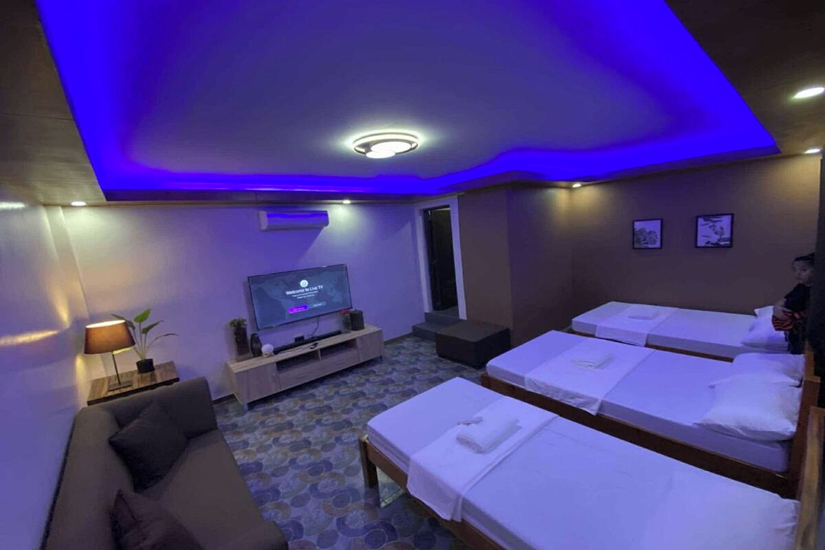 A hotel room with a TV, a sofa, and three beds.