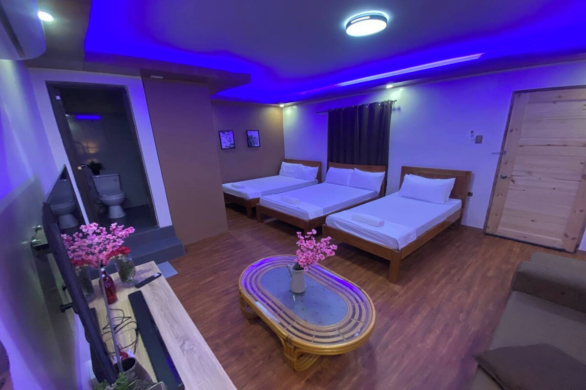 A hotel room with two beds, a wooden floor, a small table with a vase of flowers, and a television on a stand.