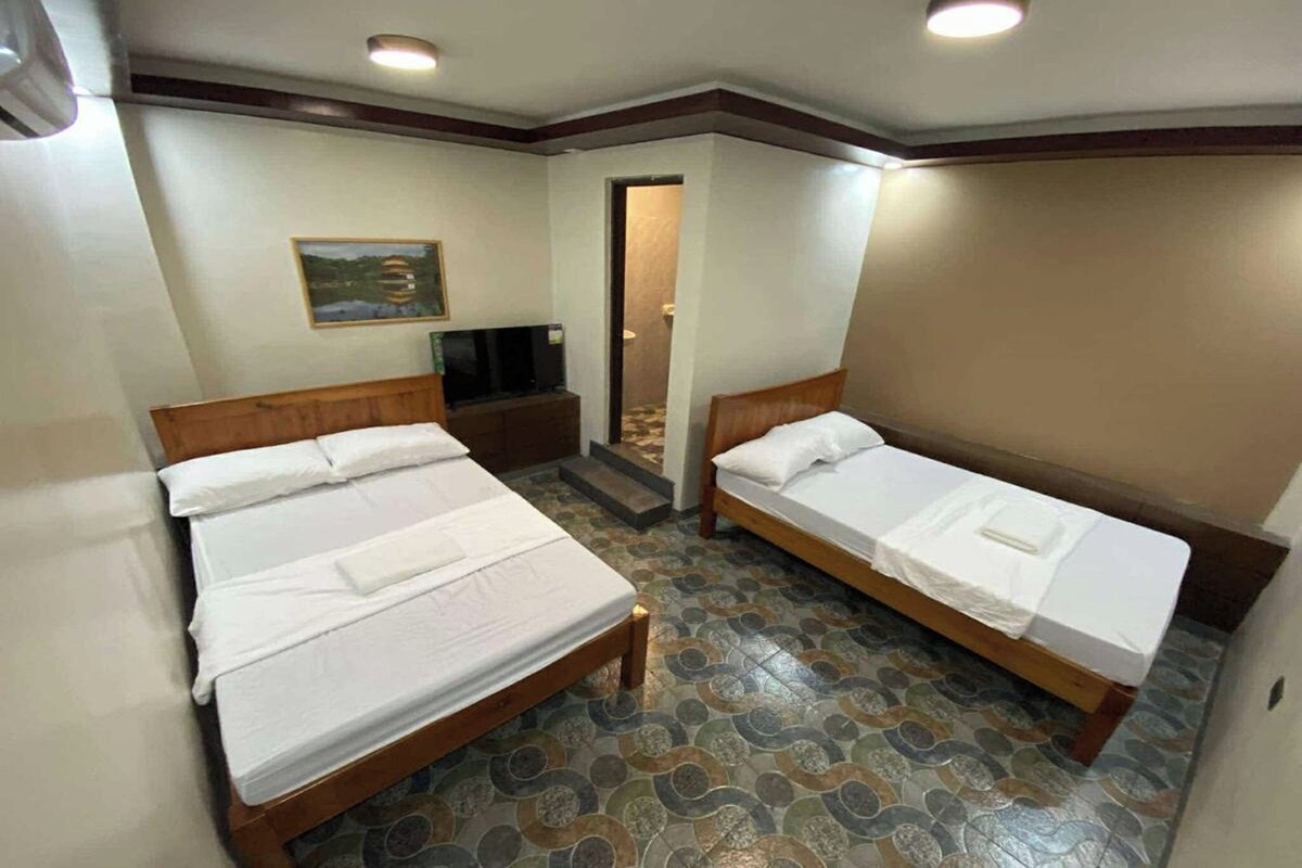 A hotel room with two single beds, a television on a nightstand, and a patterned floor.