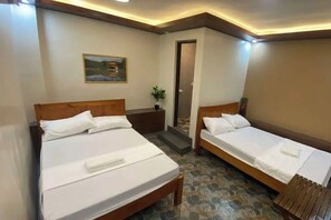 Habitación de hotel con dos camas individuales, una mesita, una mesita de noche, una puerta y un cuadro en la pared.