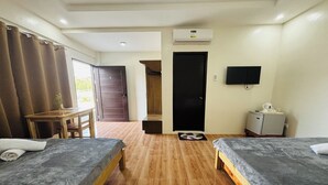 A hotel room with two beds, a wooden floor, a desk, a chair, a television, and an air conditioning unit. - Selline Bed And Breakfast (Bacnotan)
