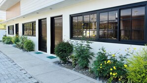 A modern building with multiple black-framed windows and doors, a clean white facade, and a well-maintained garden with yellow flowers and shrubs. - Selline Bed And Breakfast (Bacnotan)