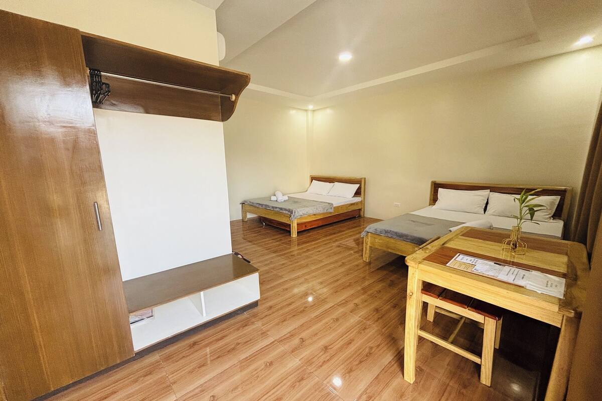 A hotel room with two beds, a wooden bench, a small table with a vase, and a wooden wardrobe.