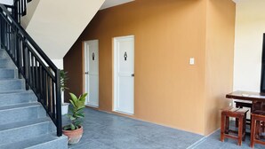 A staircase with black railings leading to a landing with two white doors, a potted plant, and a wooden table with two stools. - Selline Bed And Breakfast (Bacnotan)