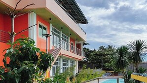 Un edificio de dos pisos con fachada roja, un balcón y una zona de piscina.