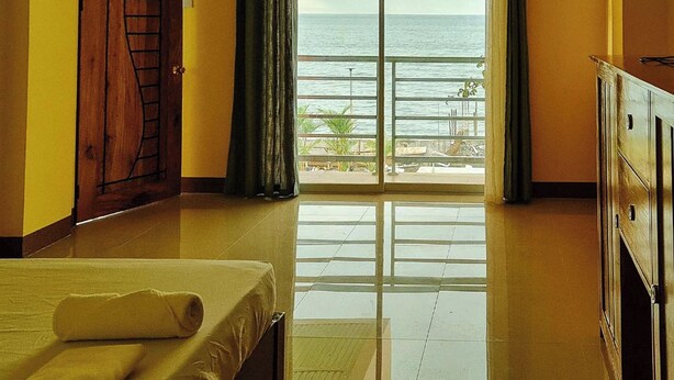 Habitación de hotel con cama, armario de madera, balcón con vista al mar y puerta con diseño decorativo.