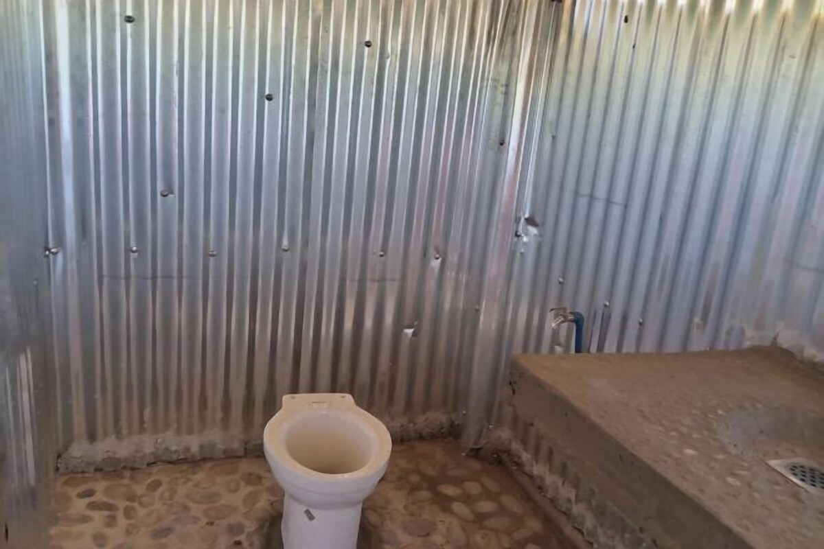 A small, enclosed bathroom with a toilet, a concrete bench, and a corrugated metal wall.