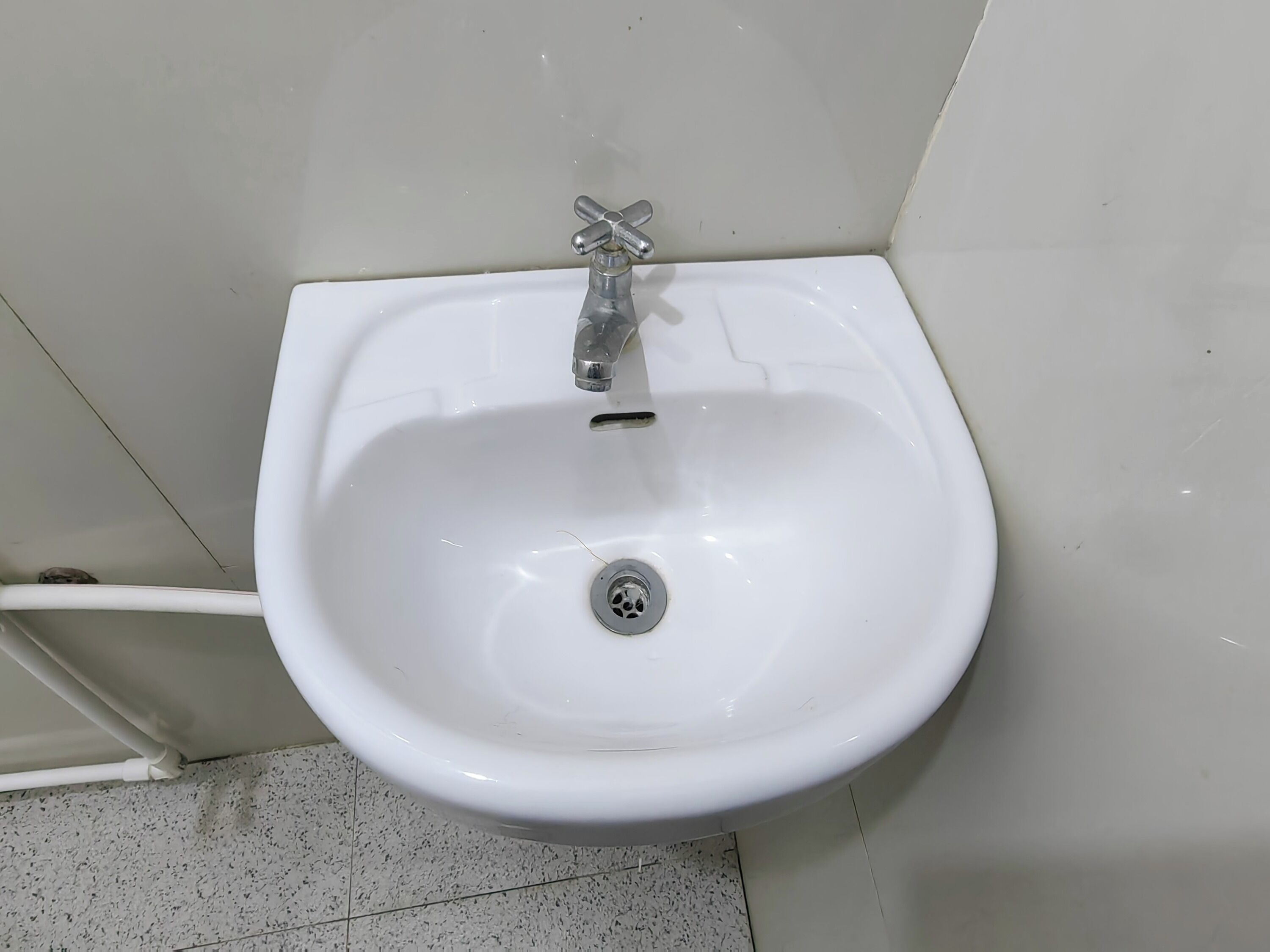 A white bidet with a chrome faucet and a drain in a bathroom with white tiled walls and floor.