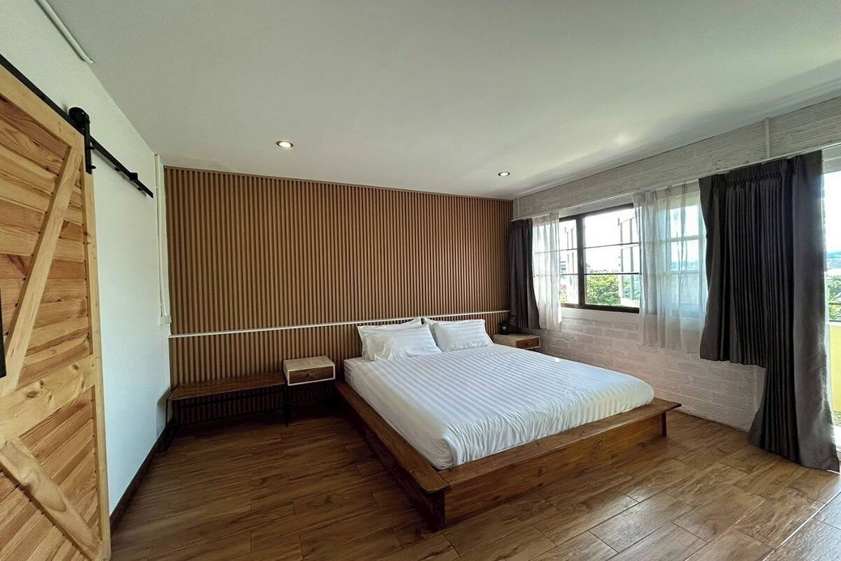 A modern bedroom with a wooden bed frame, a slatted wooden wall, and a large window with curtains.