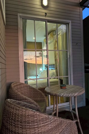 A room with a sliding glass door leading to a balcony, wicker furniture, and a bed with a floral bedspread. - Norn-Nanta House (Chiang Mai)