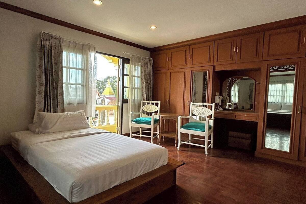 A bedroom with a bed, a desk, and a chair. There is a window with curtains and a view of the outside.