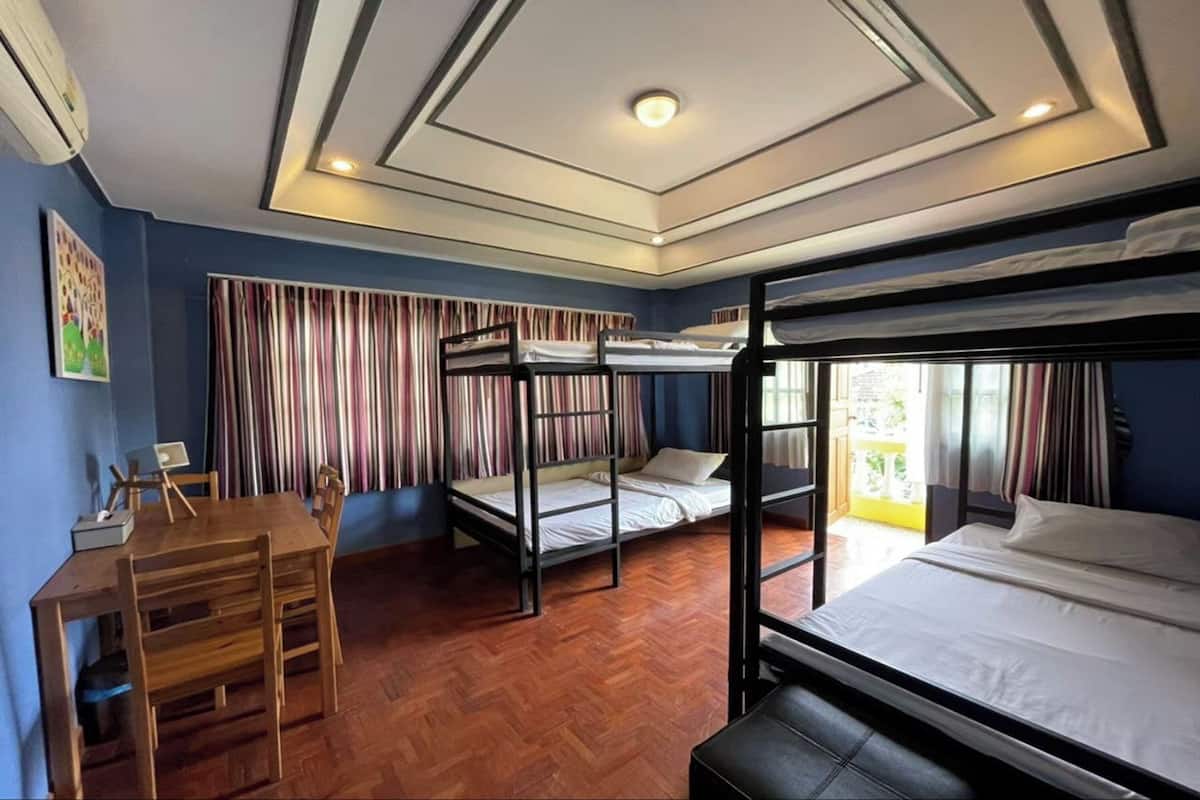 A dormitory room with bunk beds, a wooden table with chairs, and a window with striped curtains.