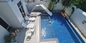 A swimming pool with tiled flooring, a slide, and white lounge chairs. - Bm Pool Villa Pattaya (Sattahip)